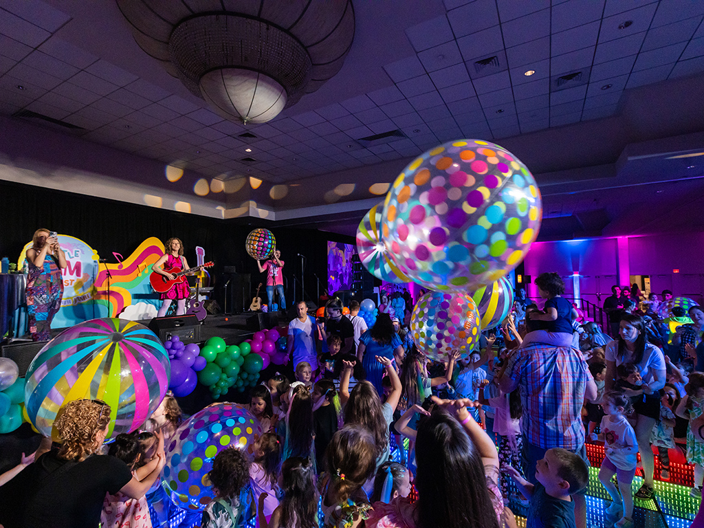 A lively crowd at the 1st Annual Little Jam Fest, enjoying energetic live performances, interactive family activities, and engaging music sessions at the Miami Beach Convention Center’s Sunset Vista Ballroom. Children dance to the beats, families sing along, and beloved characters entertain attendees, creating an unforgettable community celebration.